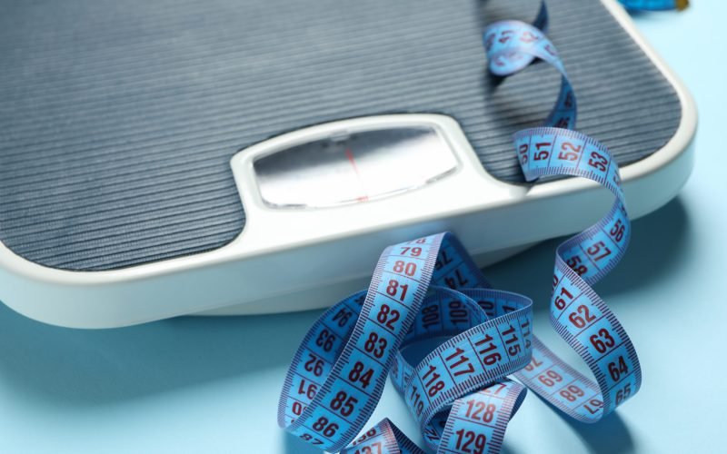 Scales and measuring tape on blue background. Weight loss concept